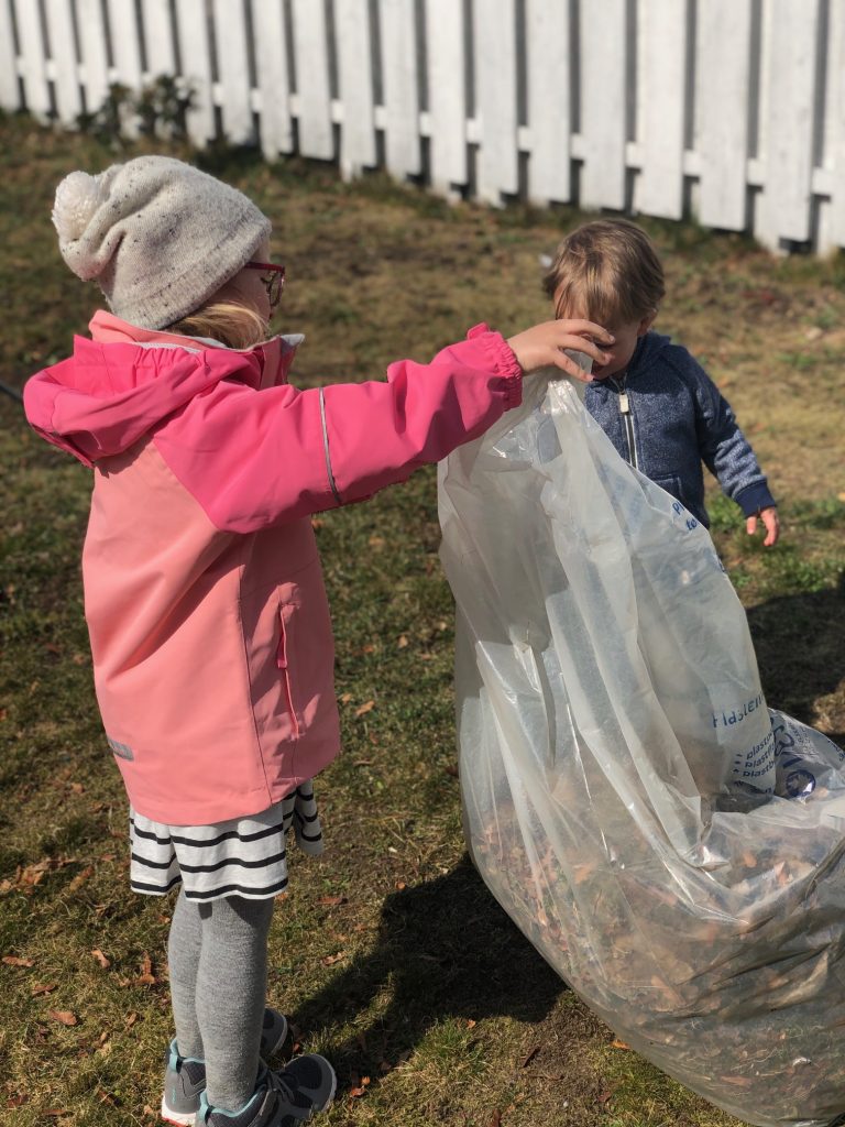 Jente og gutt som holder klar søppelsekk i hage