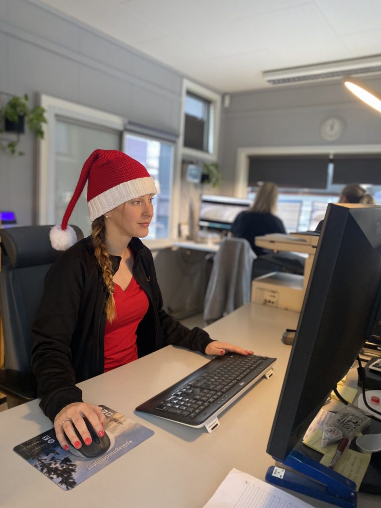 Kvinne med julenisselue som sitter ved en kontorpult og ser inn i PC-skjerm