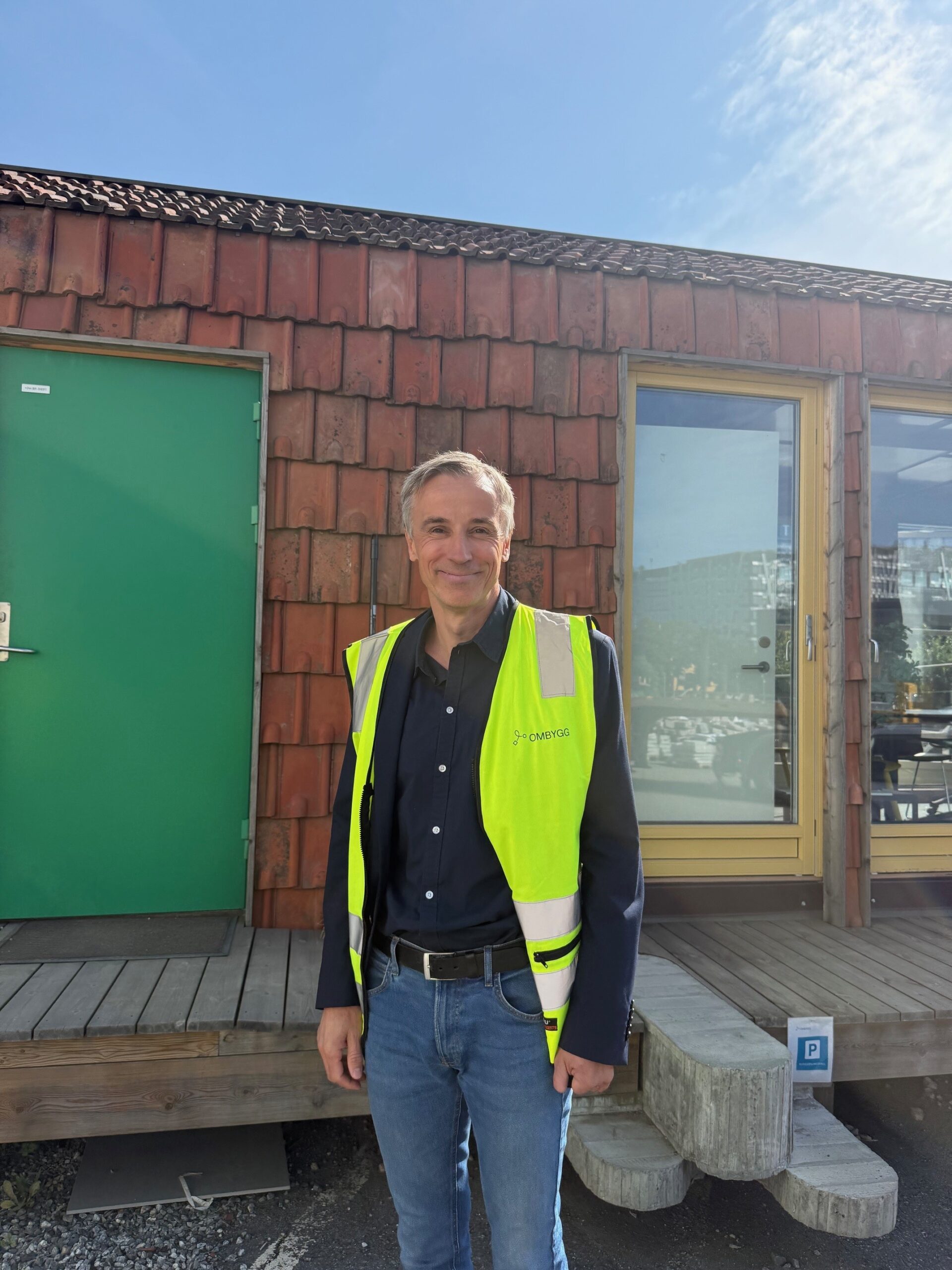 Mann i gul refleksvest som smiler utenfor et bygg